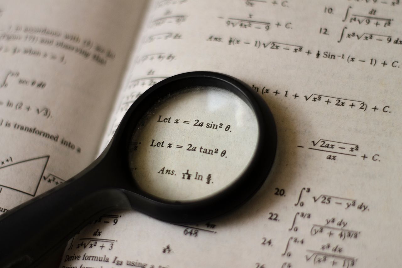 our-story A magnifying glass focusing on mathematical equations in a textbook, symbolizing detailed study.